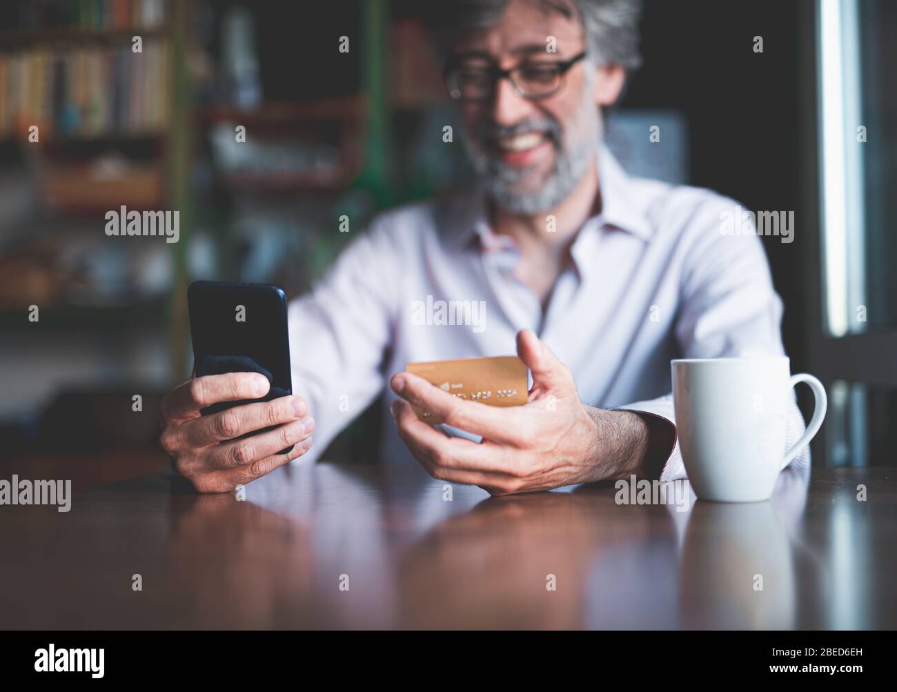 sorridente uomo con smartphone e carta di credito sta acquistando on line, concetto di e-commerce, concentrarsi sulla mano e i dispositivi, sfondo sfocato e modello Foto Stock