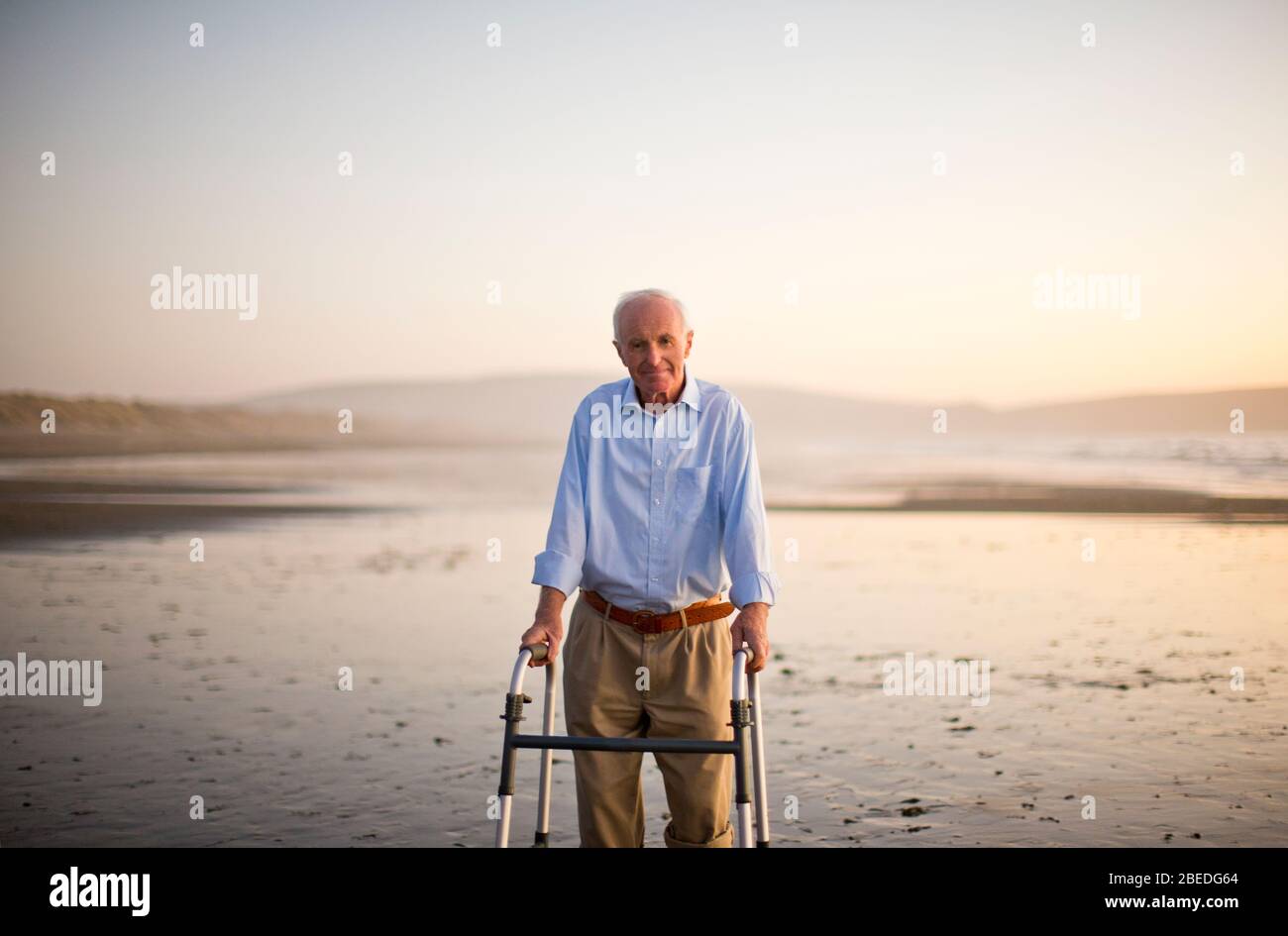 Ritratto di un anziano uomo in piedi su una spiaggia con un aiuto a piedi. Foto Stock