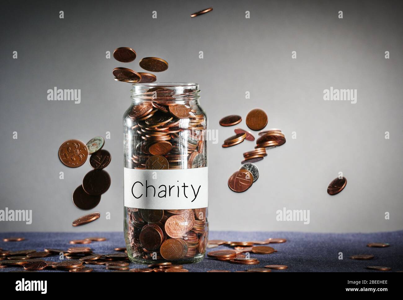 Monete che cadono su un vaso di denaro di beneficenza pieno di sterline britanniche Foto Stock