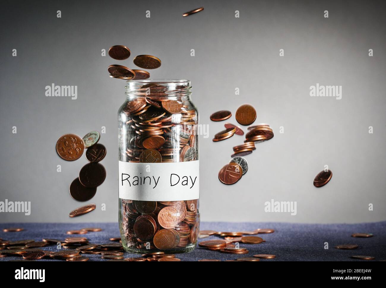 Monete che cadono su un vaso di denaro di fondo di giorno piovoso pieno di sterline britanniche Foto Stock