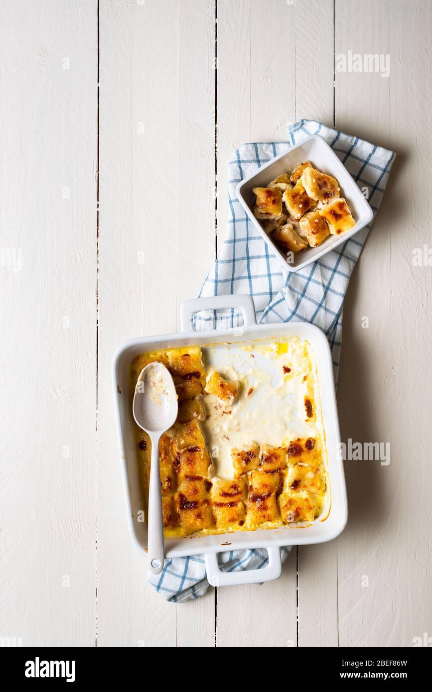 Vassoio di gnocchi al formaggio appena sfornato su tavolo bianco. Piatto con gnocchi fatti a mano con salsa di formaggio fuso. Tradizionale pasto di pasta italiana. Foto Stock