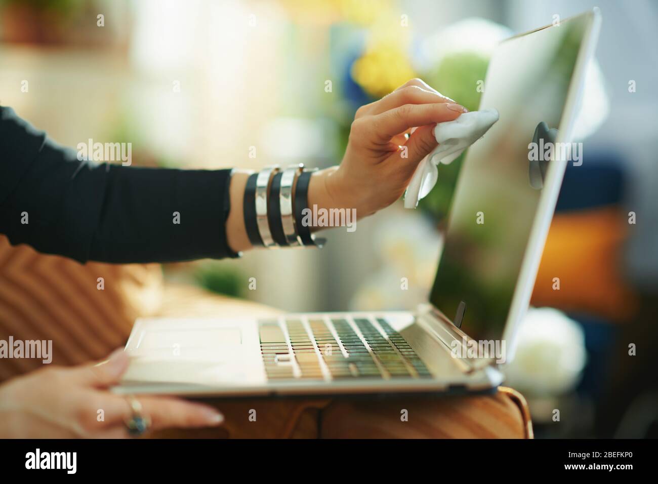 Primo piano su casalinga pulizia schermo del computer portatile con panno per la pulizia in casa in giorno di sole. Foto Stock