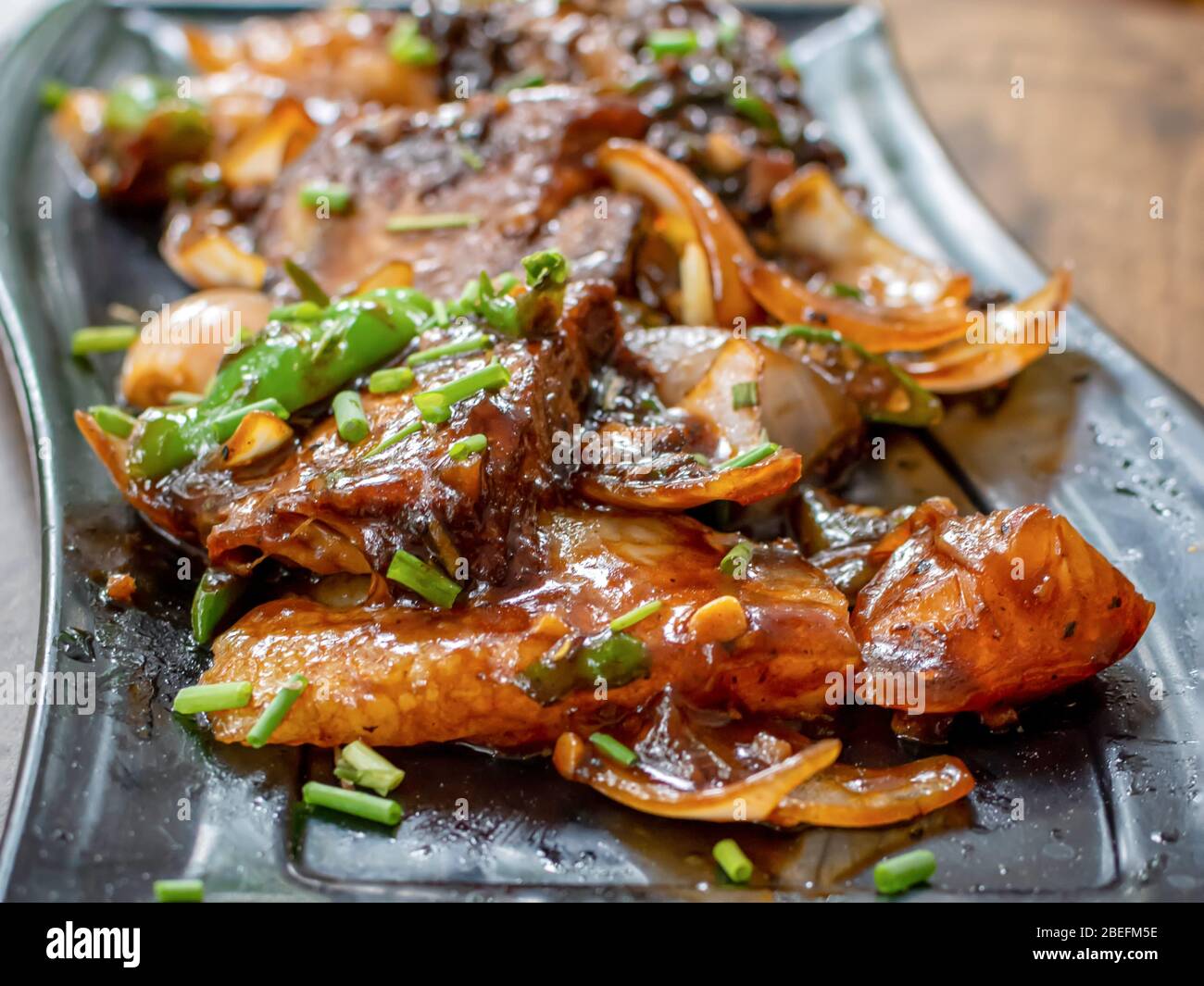 Maiale al peperoncino arrosto servito in un piatto nero su sfondo maledetto. Messa a fuoco selettiva Foto Stock