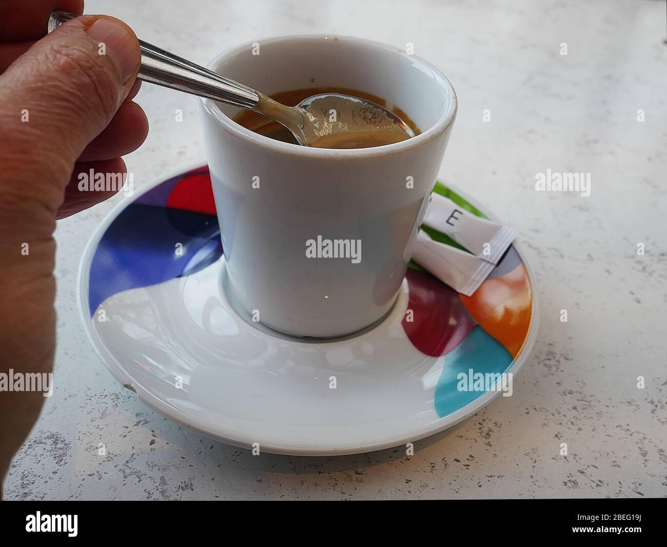 Bere un espresso servito su un piattino colorato in un bar. Cucchiaio e zucchero Foto Stock