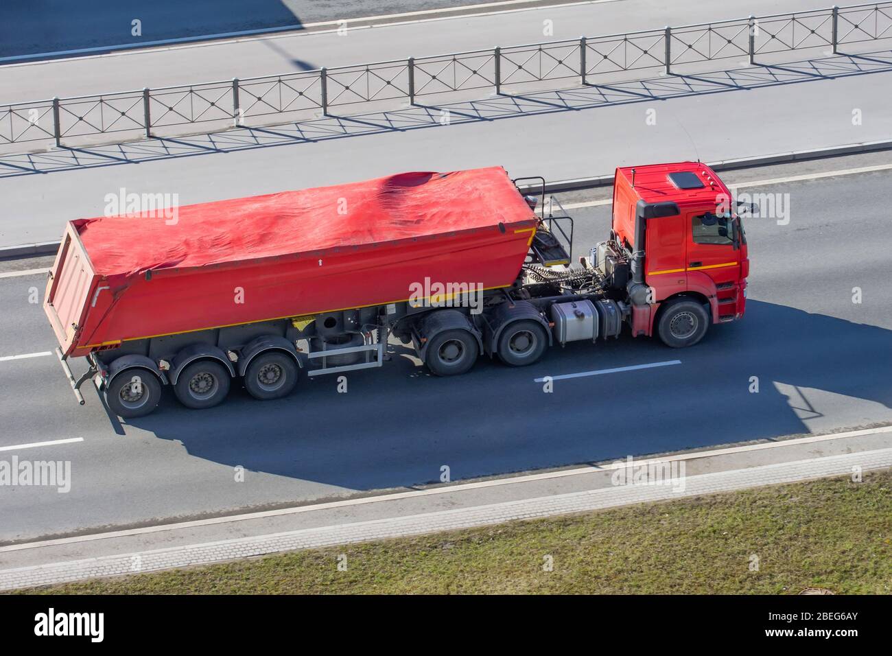 Autocarro pesante con rimorchio e carico sfuso - terreno, ghiaia, sabbia ricoperta da una tenda in gomma in tessuto corre sull'autostrada in città Foto Stock