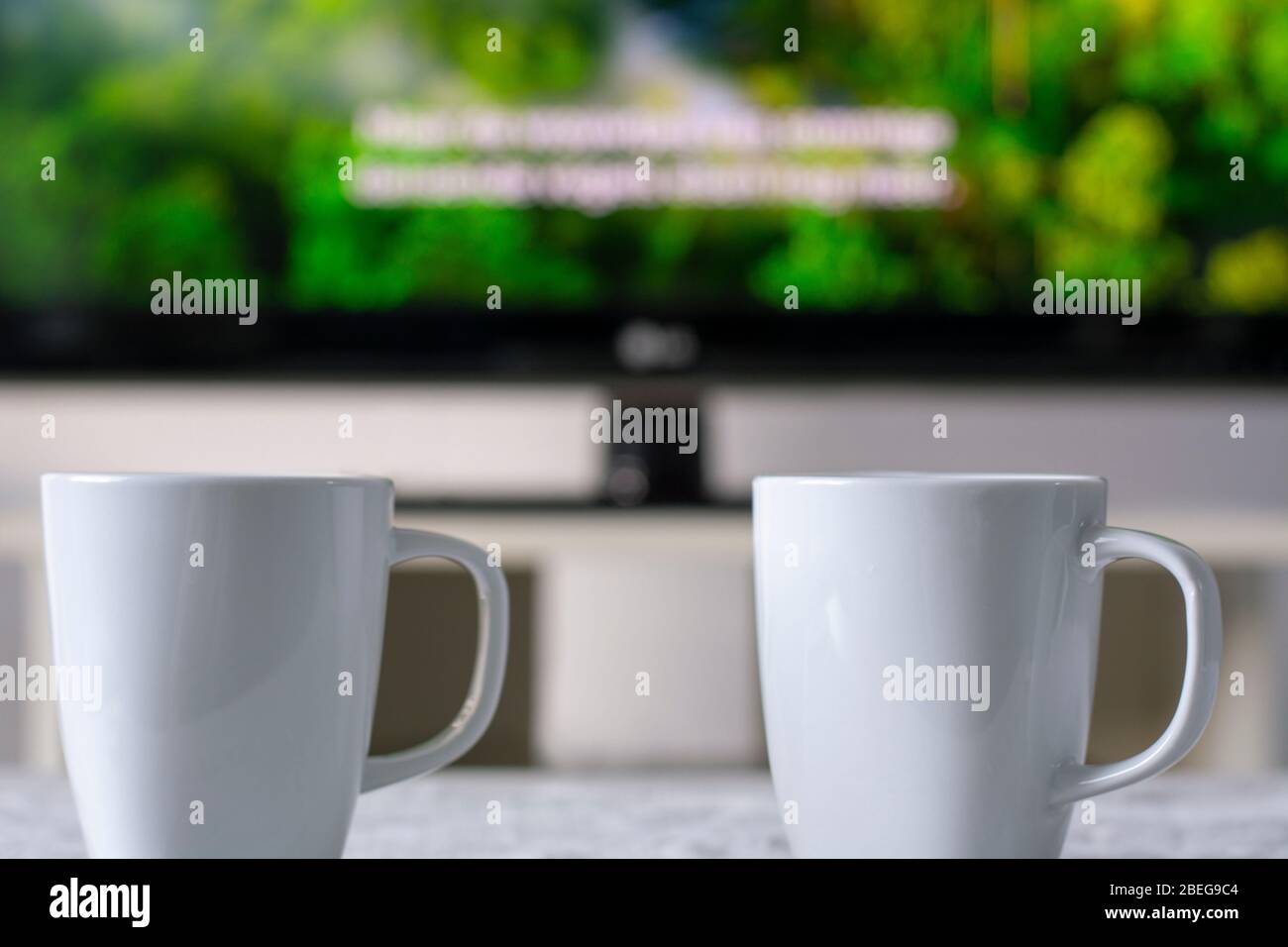 Tazze da caffè con un televisore con un documentario e sottotitoli sulla natura in background Foto Stock
