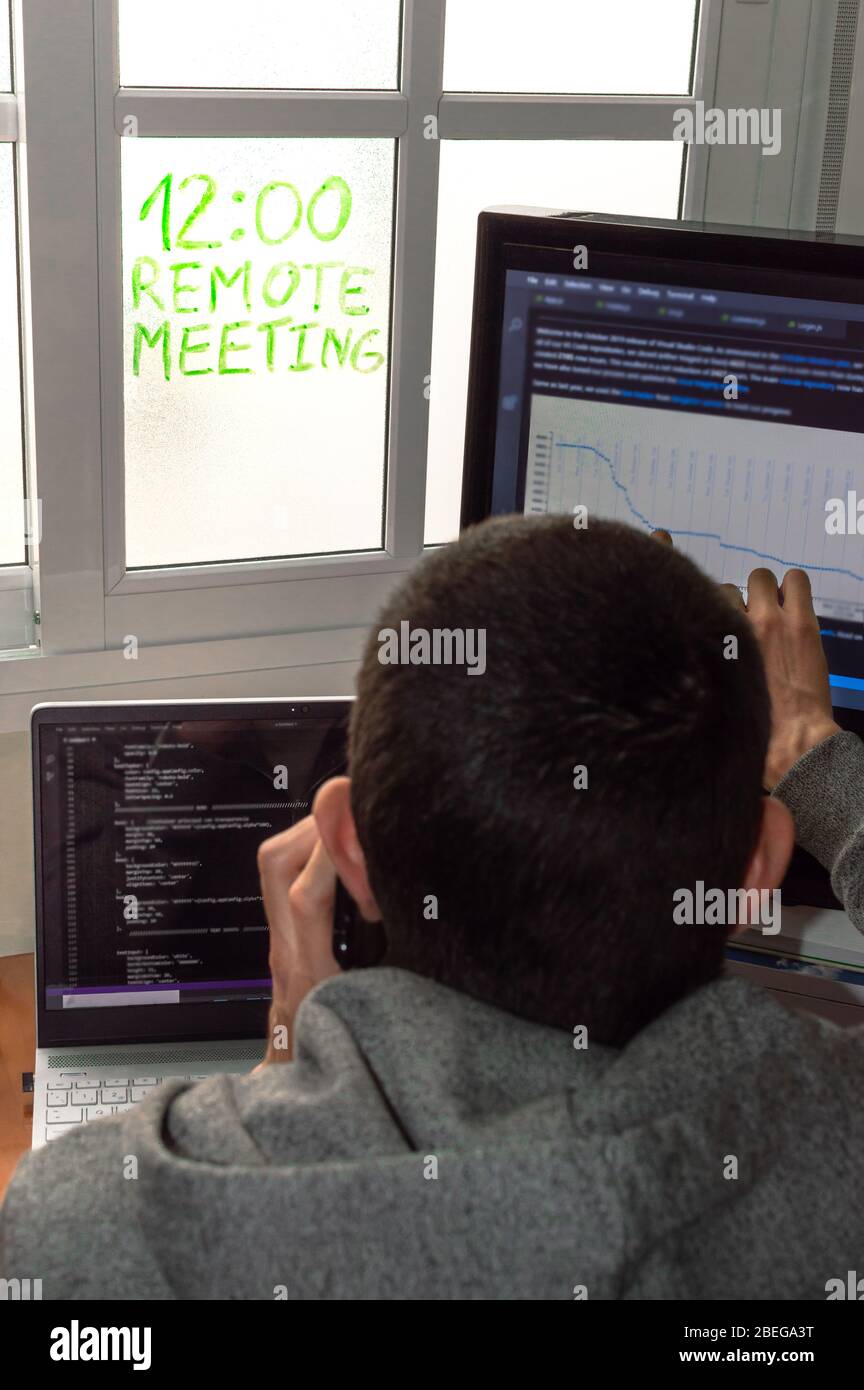 Giovane uomo che lavora a casa mentre parla al telefono in una riunione remota. Programmatore che lavora da casa. Concetto di telelavoro o telelavoro. Foto Stock