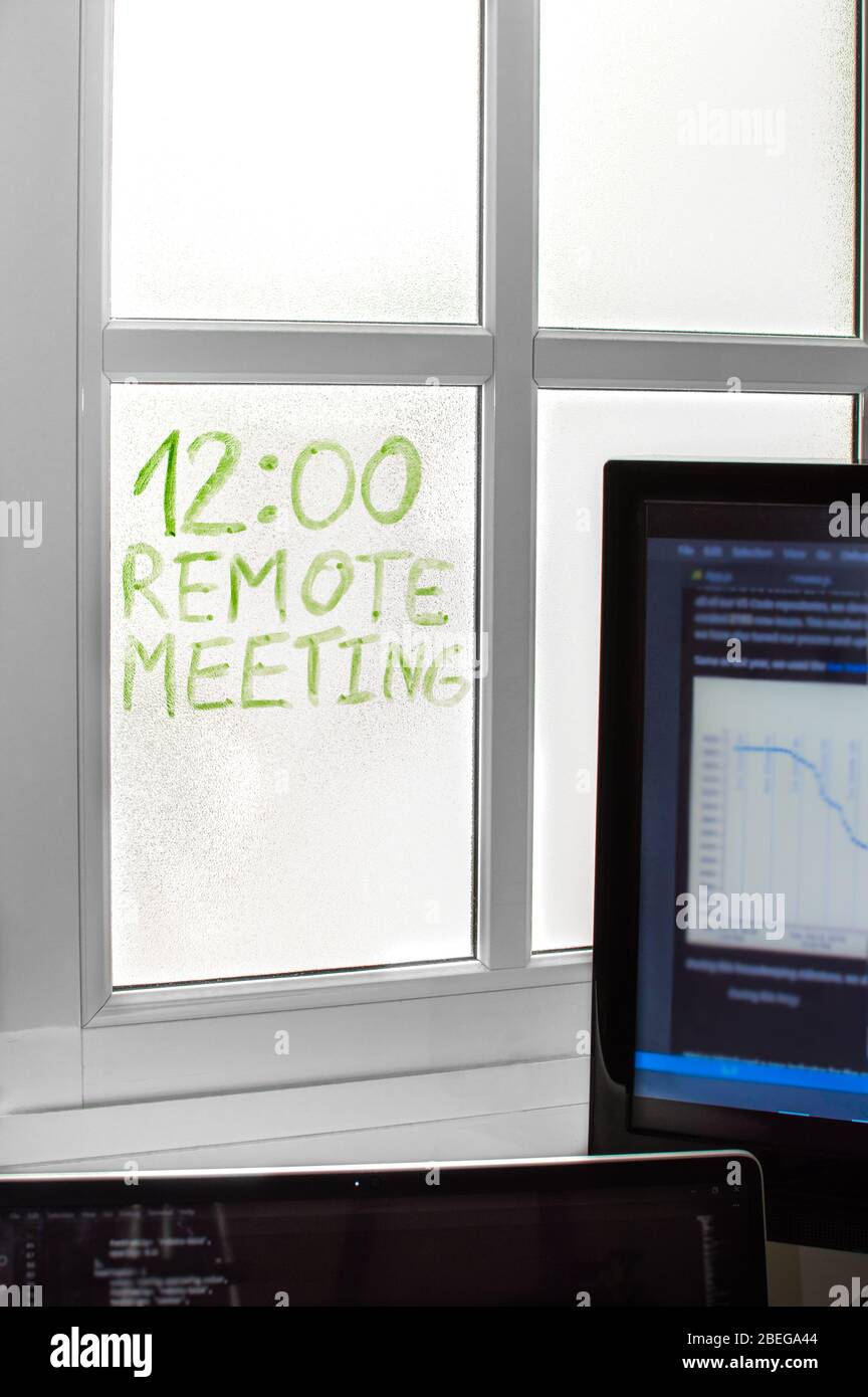 Spazio con dispositivi a casa per telelavoro, dettaglio di un promemoria scritto sulla finestra 'riunione remota'. Concetto di lavoro da casa, telelavoro. Foto Stock