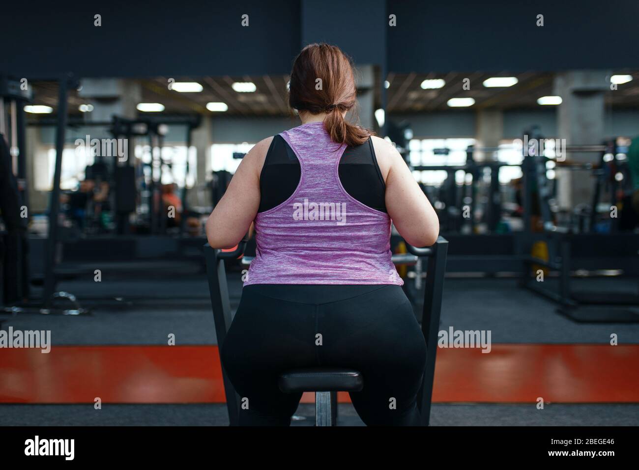 Donna in sovrappeso che fa esercizio in palestra, vista posteriore Foto Stock