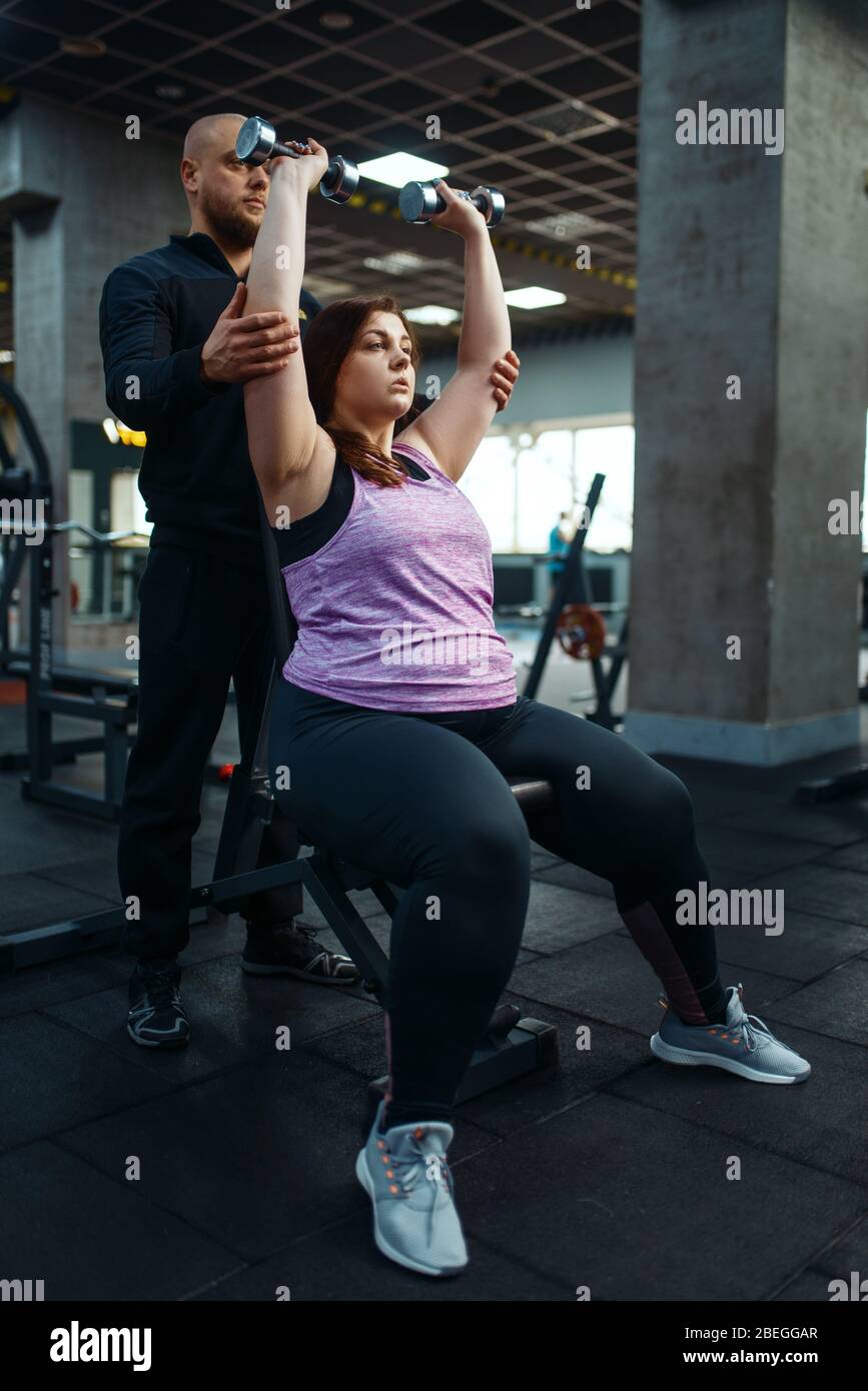Donna sovrappeso, esercizio con manubri, allenatore Foto Stock
