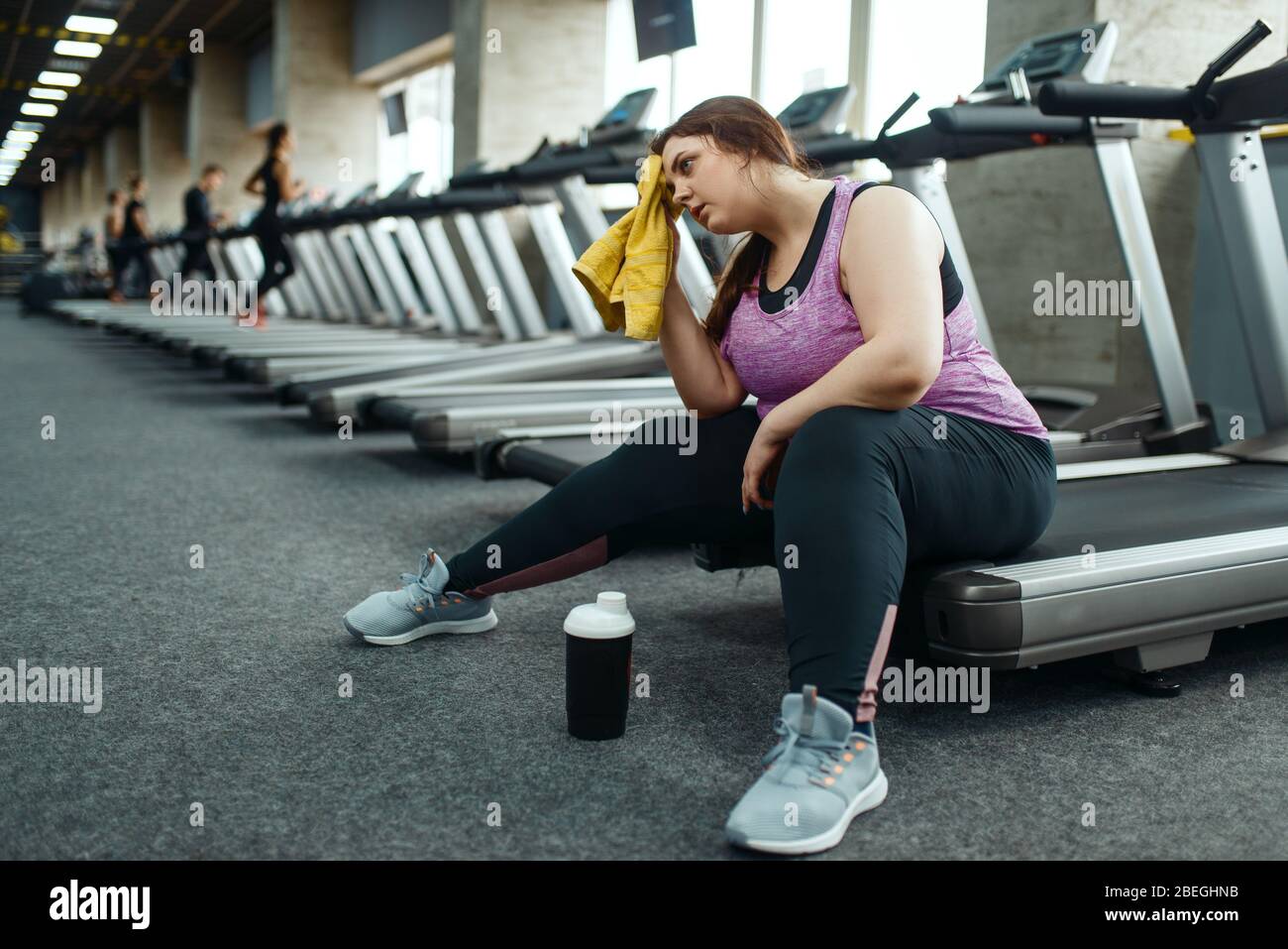 Donna stanca in sovrappeso seduta sul tapis roulant in palestra Foto Stock