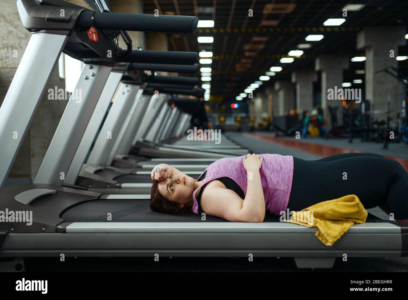 Donna stanca sovrappeso sdraiata sul tapis roulant in palestra Foto Stock