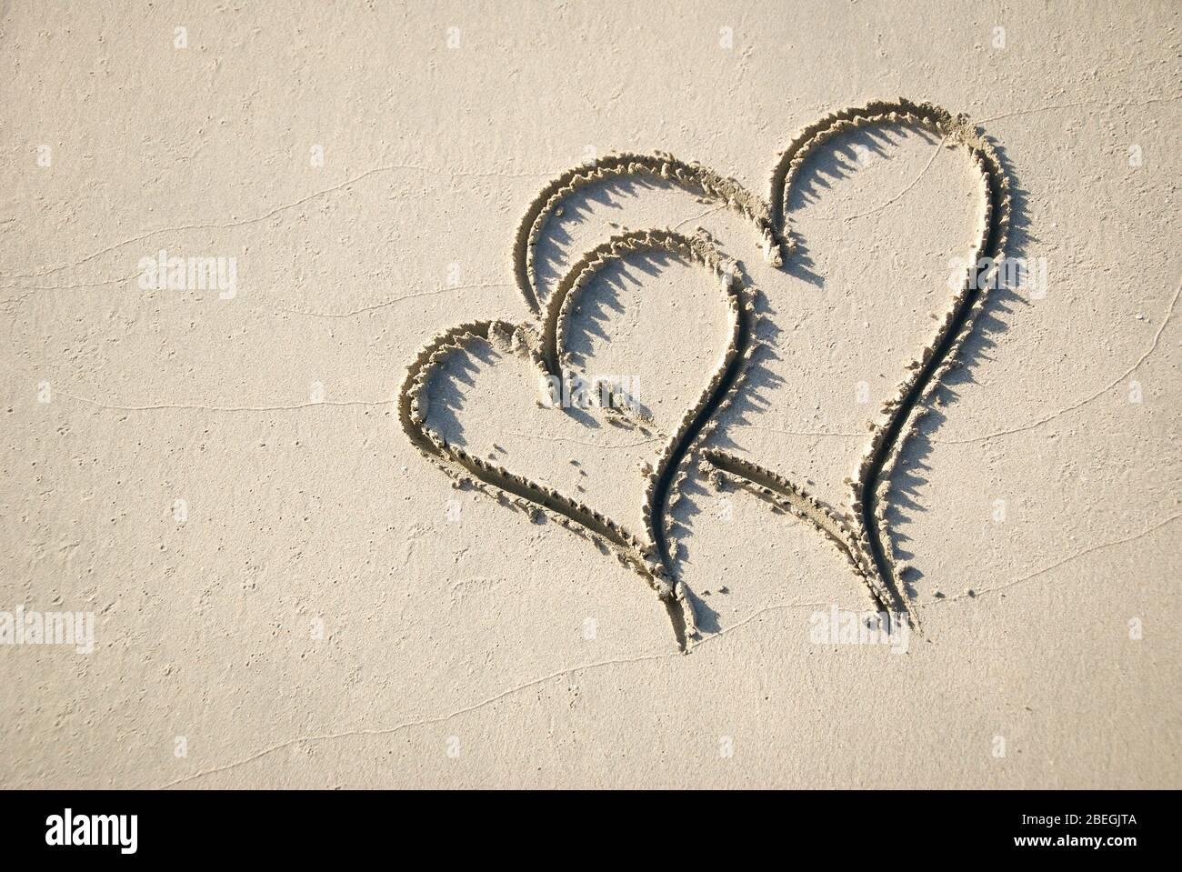 Coppia di cuori scritti a mano disegnati in un'interbloccaggio in sabbia liscia su una spiaggia soleggiata Foto Stock