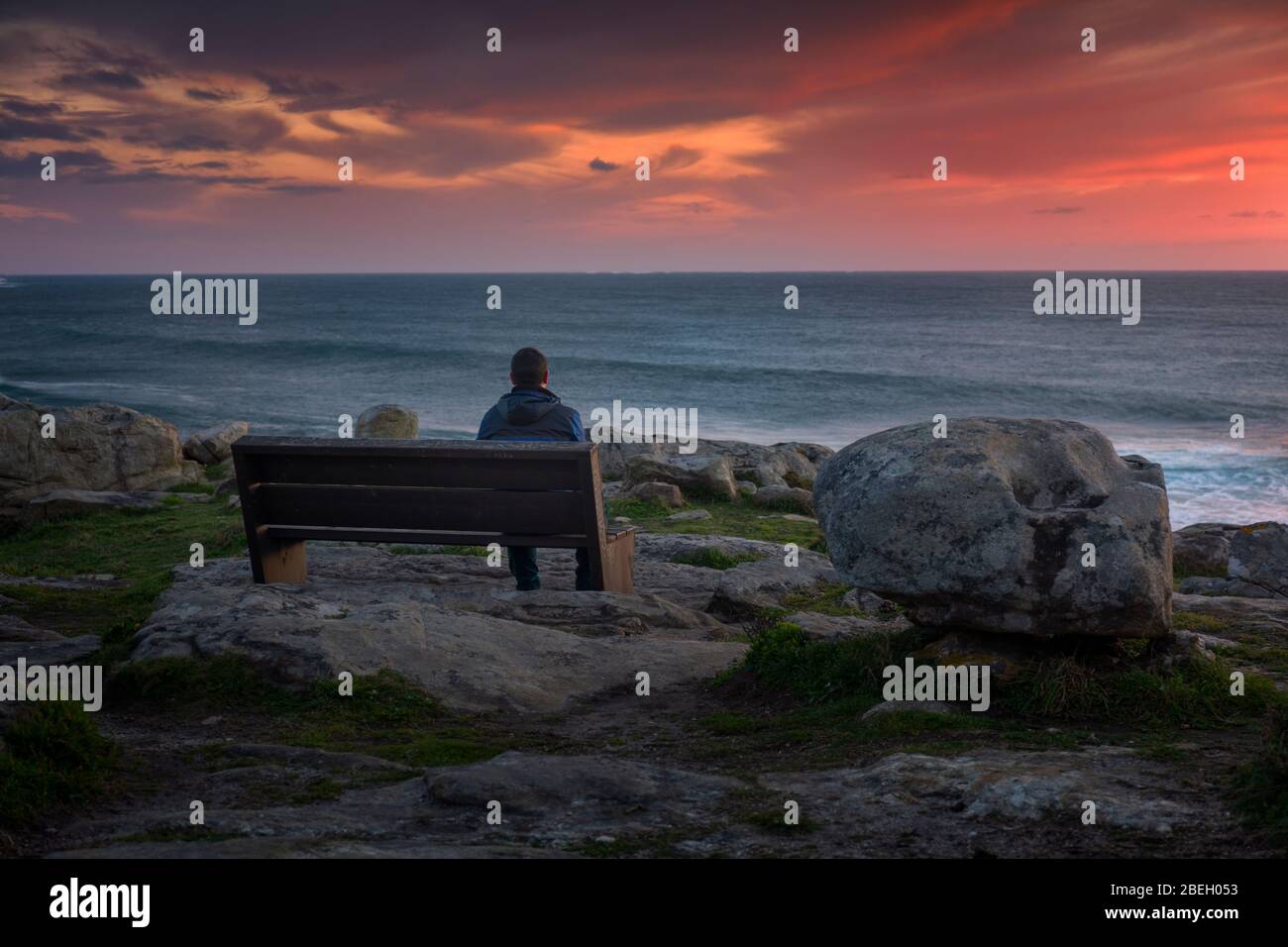 Uomo che guarda un tramonto mozzafiato seduto su una panchina sulla costa Foto Stock