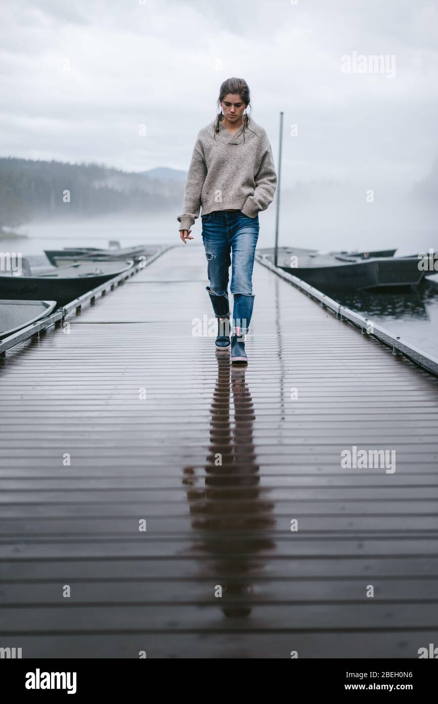 Giovane donna che cammina attraverso come molo bagnato su un lago nebbia Foto Stock