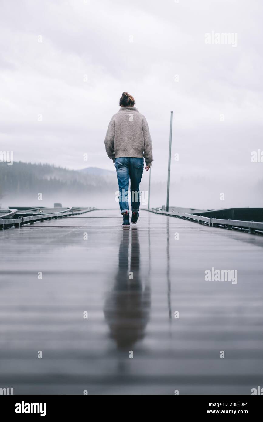 Basso angolo di giovane donna che cammina via sul molo nella nebbia Foto Stock