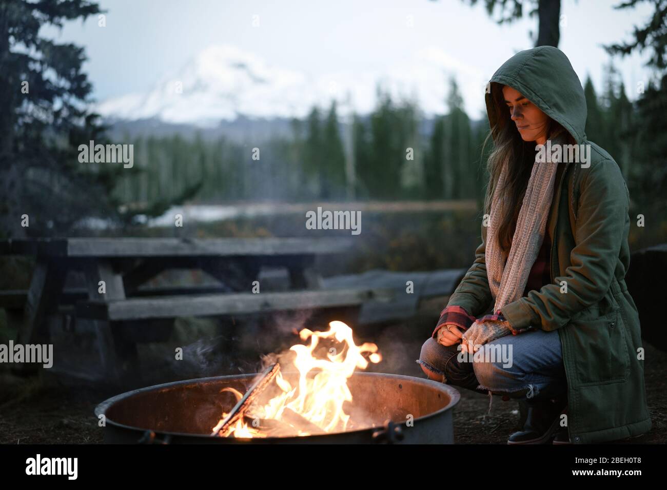 Donna accoccolata dal fuoco con cappuccio in su Foto Stock