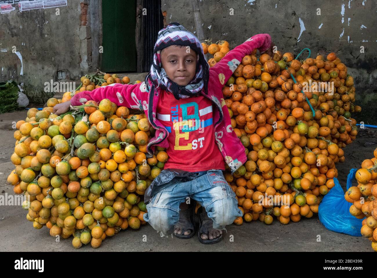 Ragazzo seduto su un mucchio di arance in un mercato locale, a sud di Cox's Bazar Foto Stock