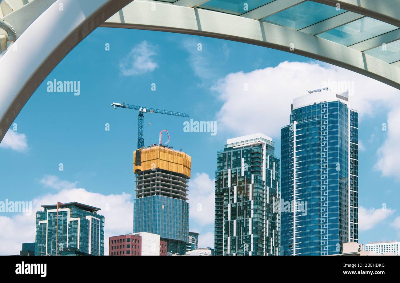 Alti e moderni grattacieli in costruzione con gru incorniciate da un arco in acciaio e vetro lungo il lungomare di Seattle, Washington Foto Stock