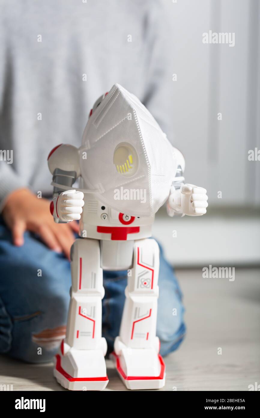 Ragazzo gioca con i suoi giocattoli, come la maschera di protezione del coronavirus e robot Foto Stock