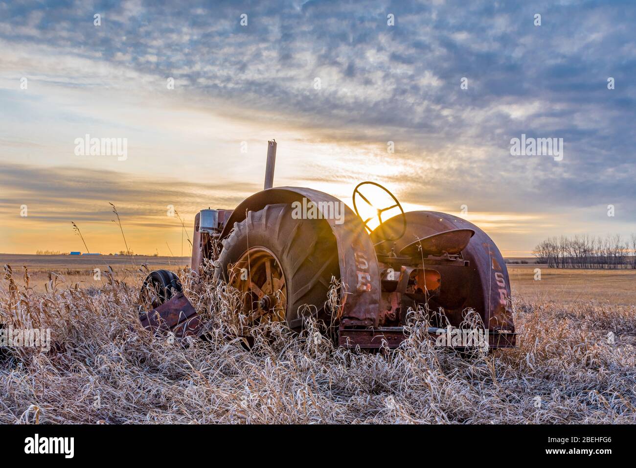 Coderre, SK- 9 aprile 2020: Sunburst al tramonto su un trattore Case d'epoca abbandonato in erba alta sulle praterie di Saskatchewan Foto Stock