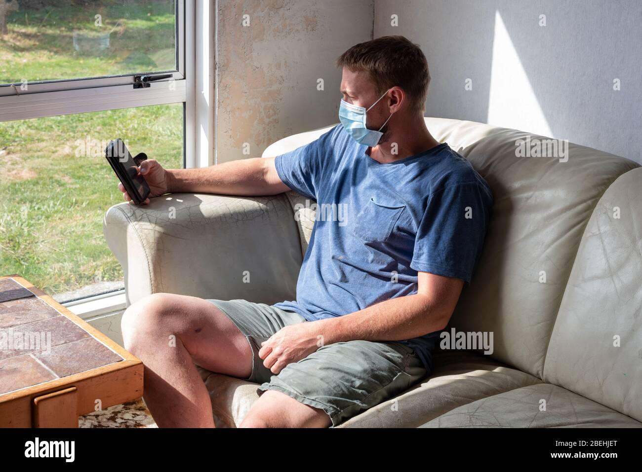 L'uomo siede da una finestra isolata indossando una maschera facciale durante la Pandemia Covid-19 del 2020 Foto Stock