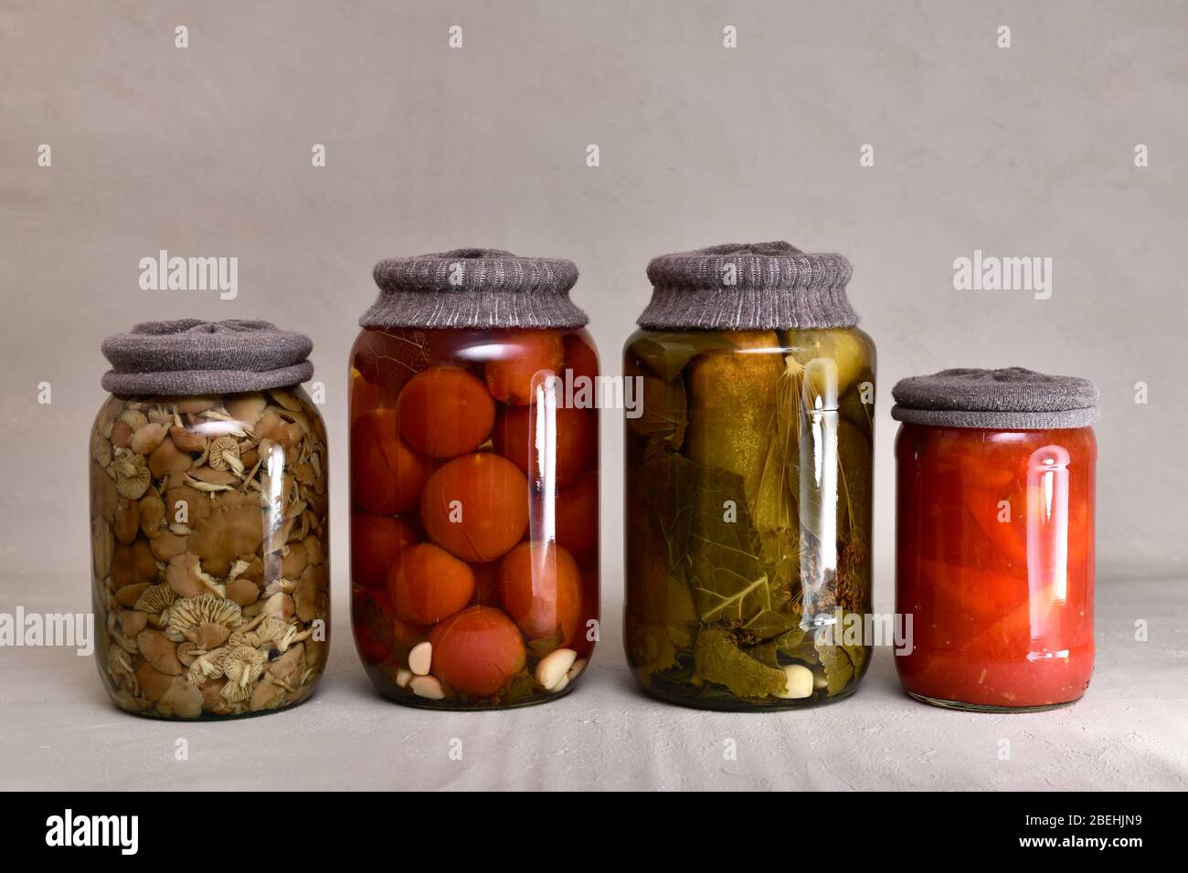 Quattro vasetti di vetro in fila con tessuto che contro la ruggine, con cetrioli fermentati, pomodori, funghi e peperoni. Foto Stock