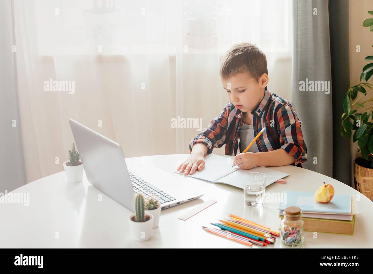 Ragazzo che studia a casa con il notebook e fa i compiti a scuola. Formazione online a distanza. Foto Stock