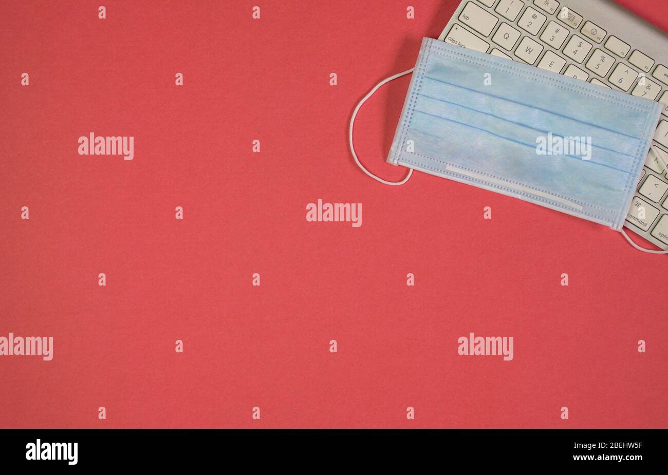 Maschera facciale medica sulla parte superiore della tastiera. Sfondo rosso. Vista dall'alto. Spazio di copia. Foto Stock