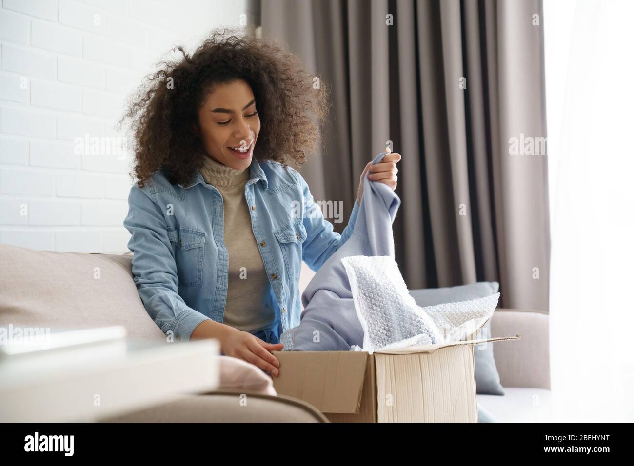 Sorpresa african giovane donna shopper disimballaggio di consegna di moda in casa. Foto Stock