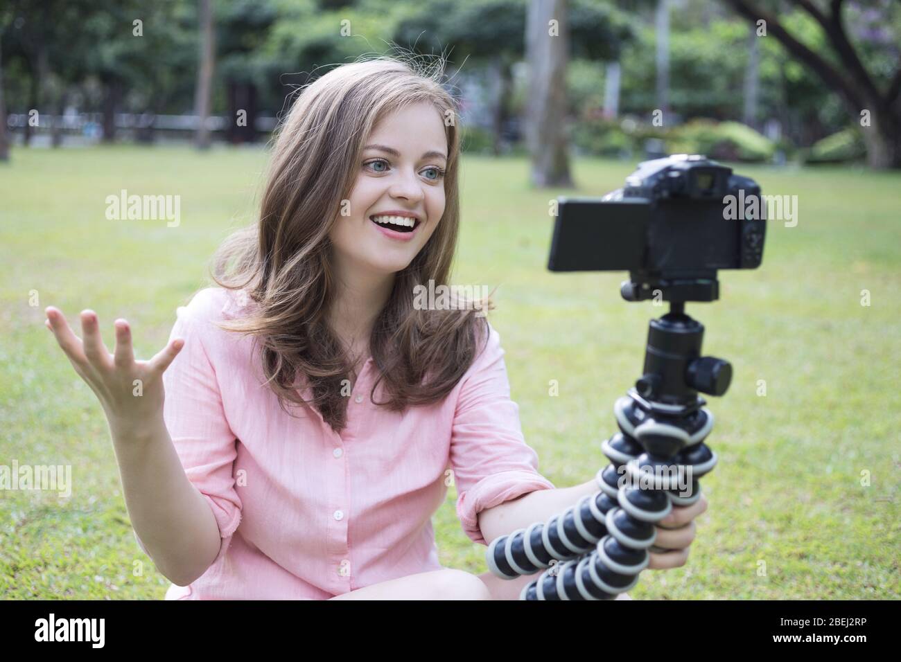 Sorridente giovane donna caucasica ragazza facendo un video blog (vlog) con fotocamera all'esterno in parco verde Foto Stock