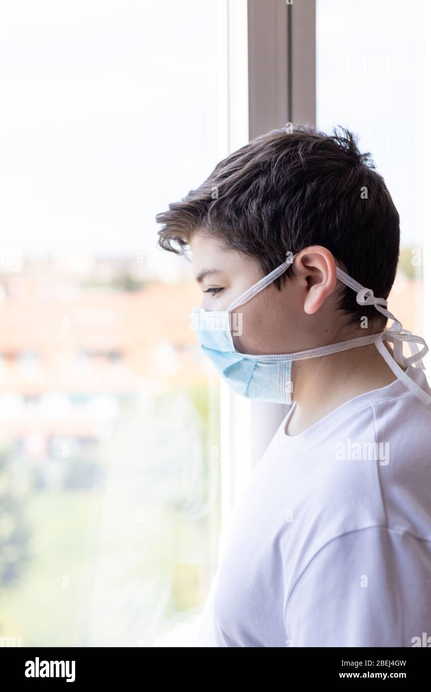 ragazzo con maschera protettiva e guanti blu che guardano fuori dalla finestra durante la quarantena del coronavirus Foto Stock