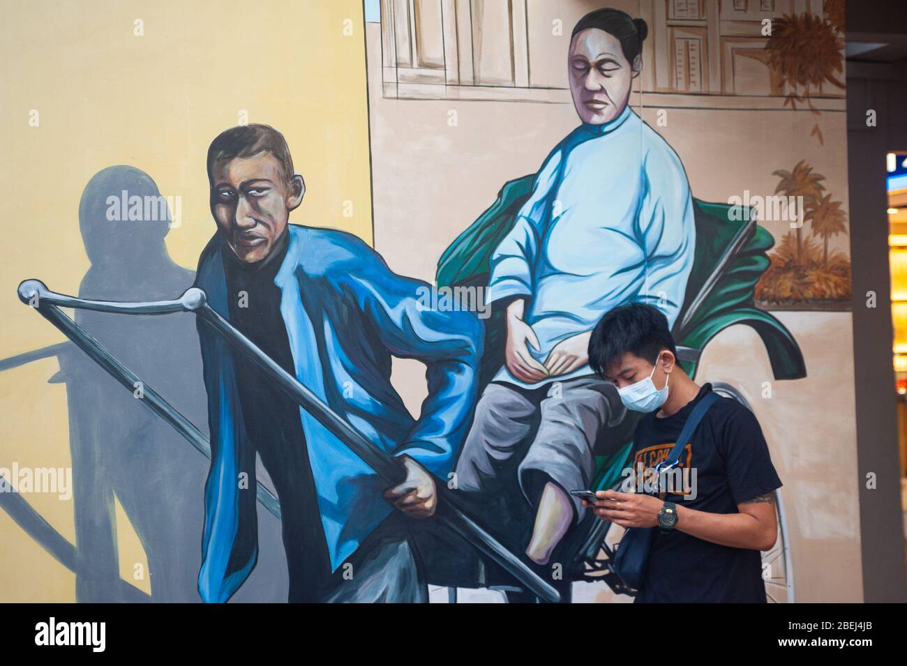 25.03.2020, Singapore, Repubblica di Singapore, Asia - UN giovane uomo con maschera facciale si erge di fronte a un murale a muro raffigurante un tradizionale risciò. Foto Stock