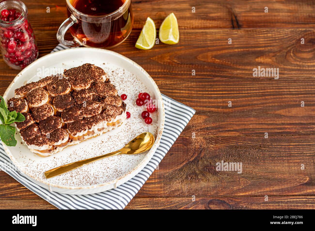 Tiramisù. Tradizionale dessert italiano su sfondo legno. Guarnito con un rametto di menta e fette di lime. In una tazza trasparente, tè con il buccia di mare. Foto Stock