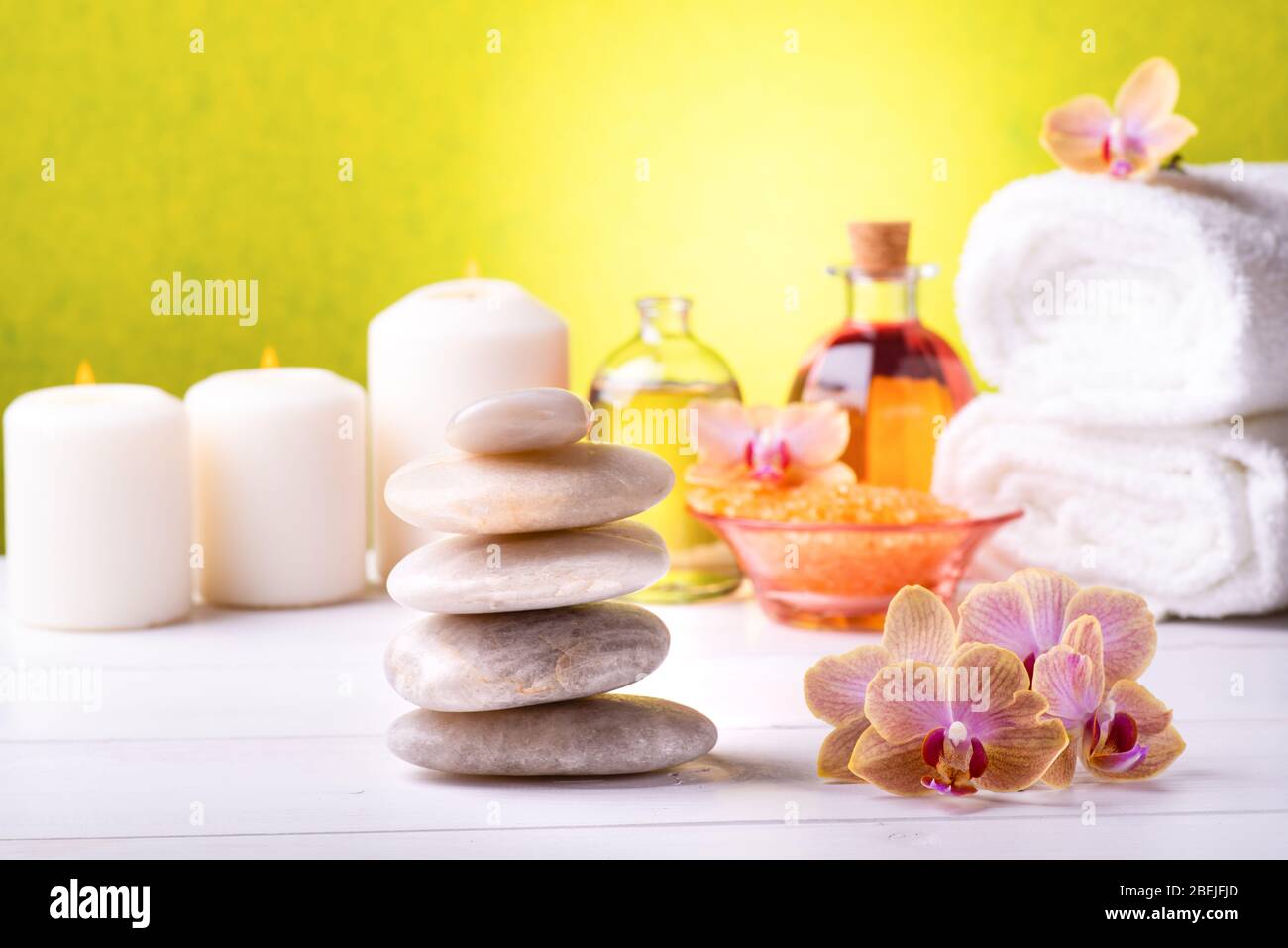 Al centro del tavolo bianco si trovano le orchidee e le pietre impilate, sullo sfondo, asciugamani bianchi, sali da bagno, alcune candele e bottiglie trasparenti Foto Stock