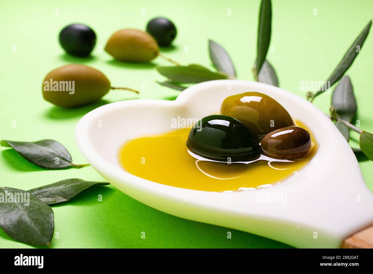 in primo piano, nel cucchiaio bianco a forma di cuore alcune olive con olio extra vergine di oliva Foto Stock