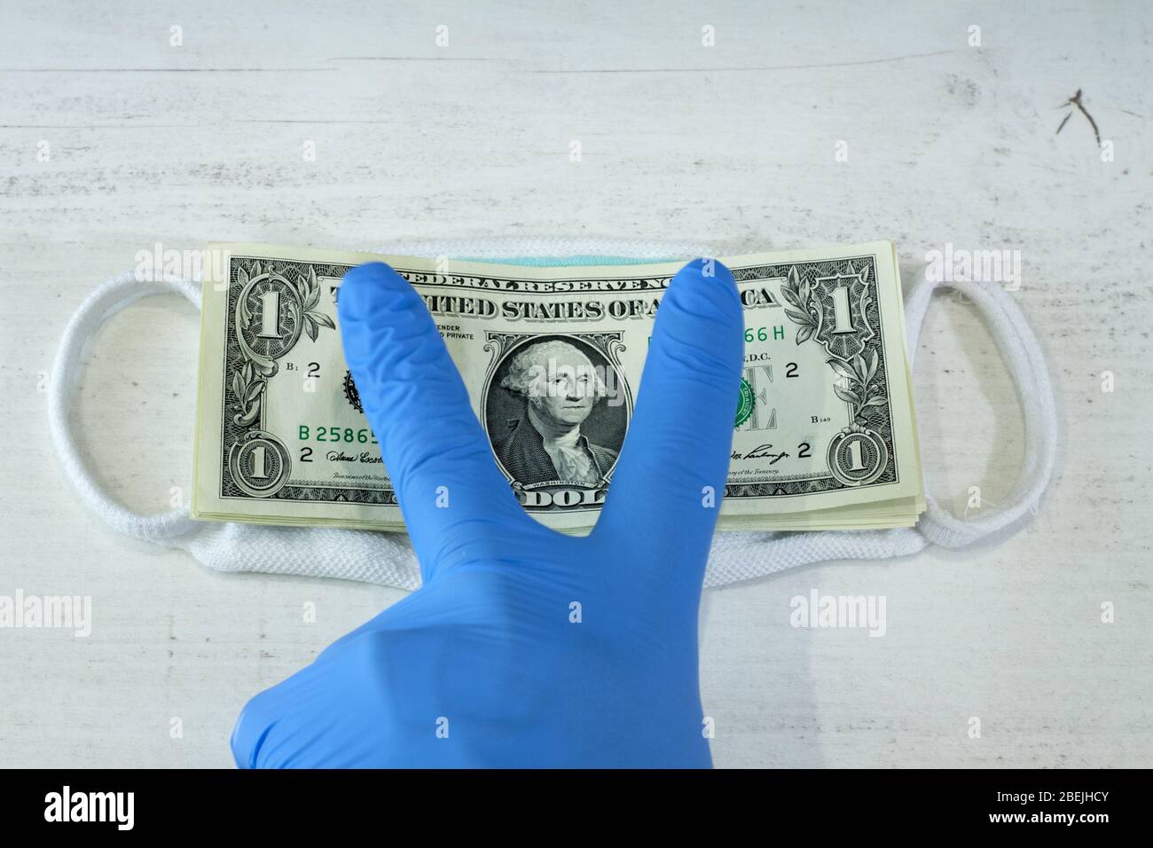 Guanti protettivi per proteggere contro il denaro di Coronavirus COVID-19. Mano umana in un guanto protettivo blu contenente un fascio di banconote e protoni Foto Stock