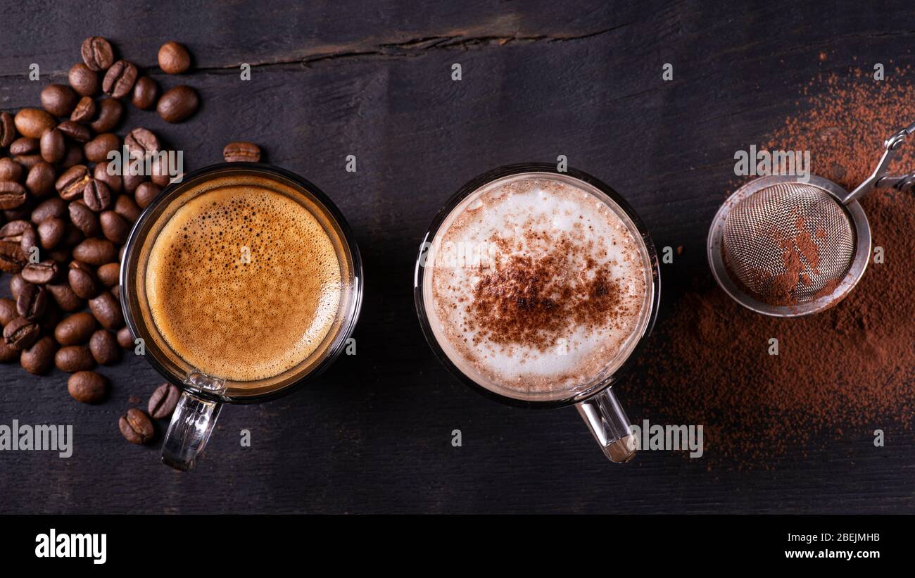 vista dall'alto, primo piano, su sfondo di legno scuro, alcuni tipi di bevande a base di espresso, latte macchiato e cappuccino con una spolverata di cacao in polvere Foto Stock