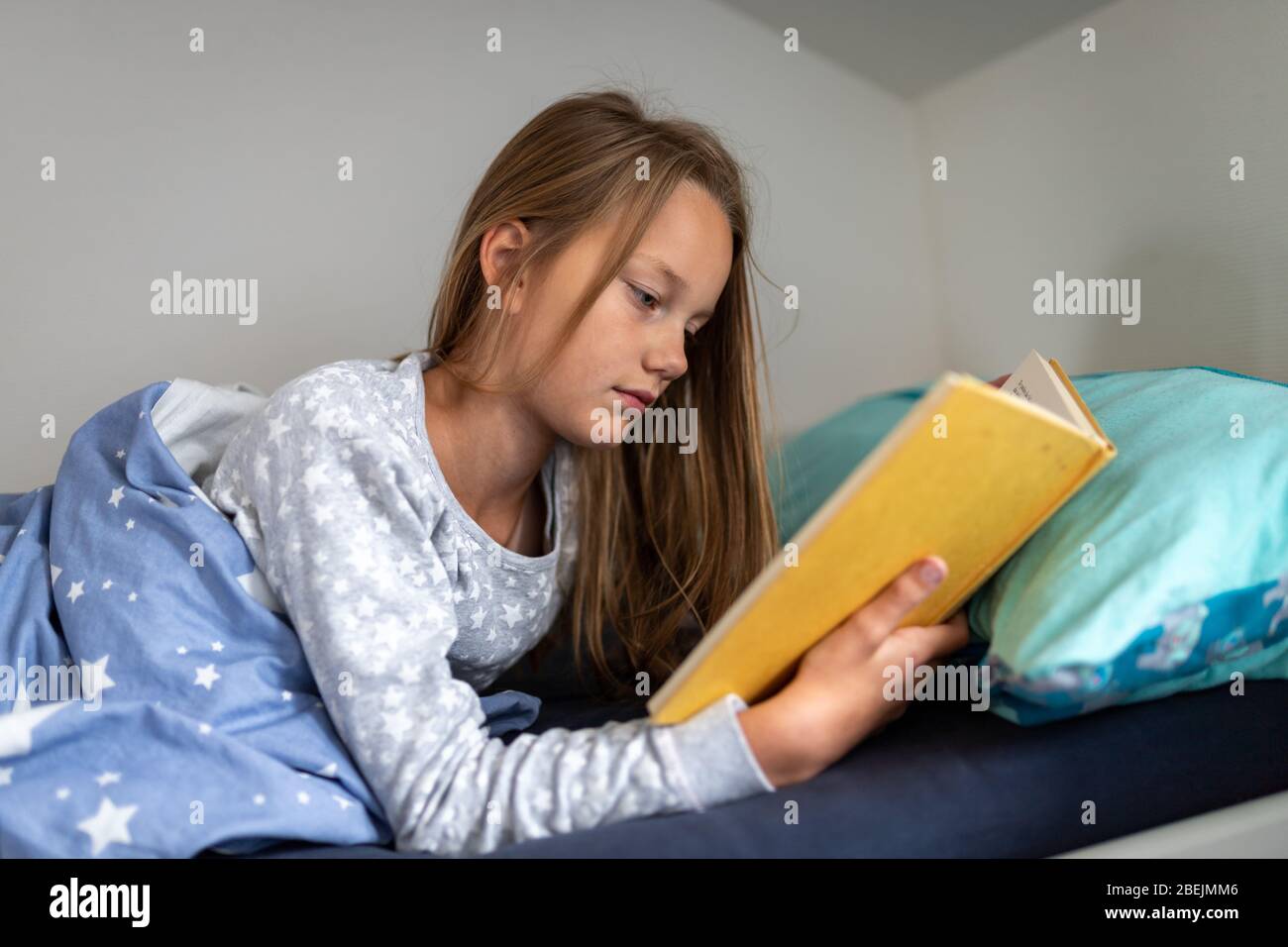 La ragazza sta leggendo un libro nel letto Foto Stock