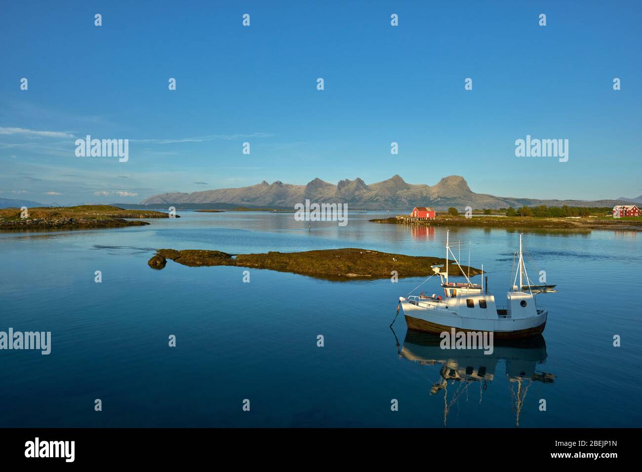 Una barca da pesca solista ormeggiata nel mare ancora estivo di South Heroy e Alsta e la catena montuosa delle sette Sorelle in Helgeland Nordland Norvegia Foto Stock