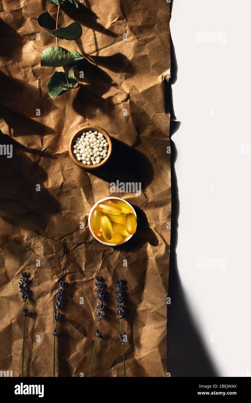 Vista dall'alto sulle capsule di olio di pesce e le palle omeopatiche giacciono su carta da imballaggio stropicciata. Circondato da rametti di eucalipto e lavanda. Foto Stock