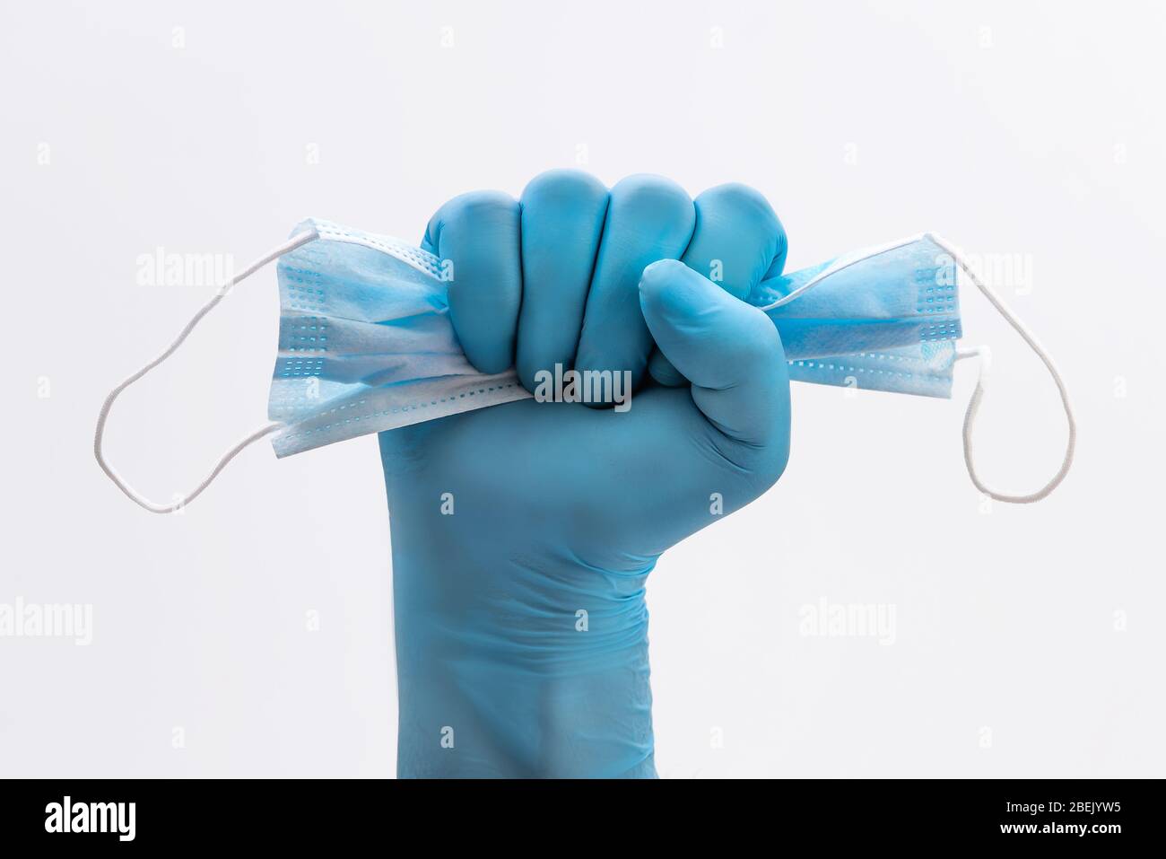Mano di Fist in guanti protettivi di lattice blu medico che tiene una maschera medica come segno di resistenza alla pandemia - su sfondo bianco. Stop malattia segno Foto Stock