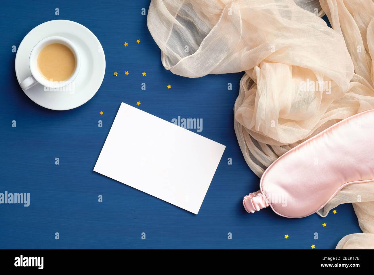 Concetto di Happy Morning. Composizione piatta con tazza di caffè, maschera per il sonno, coperta e carta vuota su sfondo blu scuro Foto Stock