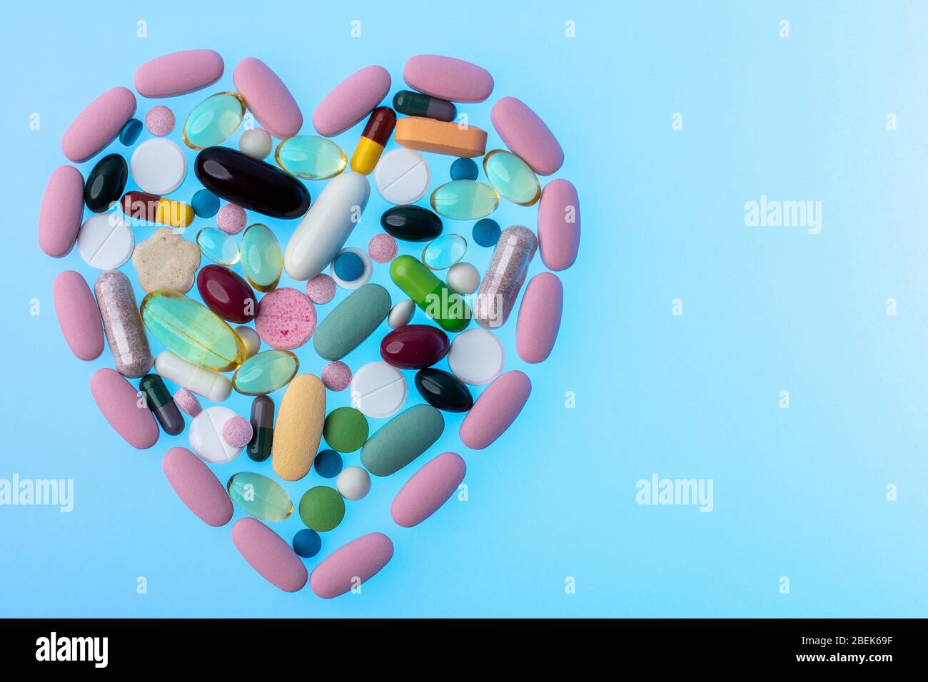 Pillole multicolore a forma di cuore su sfondo blu gradiente. Forma cardiaca in compresse, concetto di trattamento e assistenza sanitaria. Primo piano Foto Stock