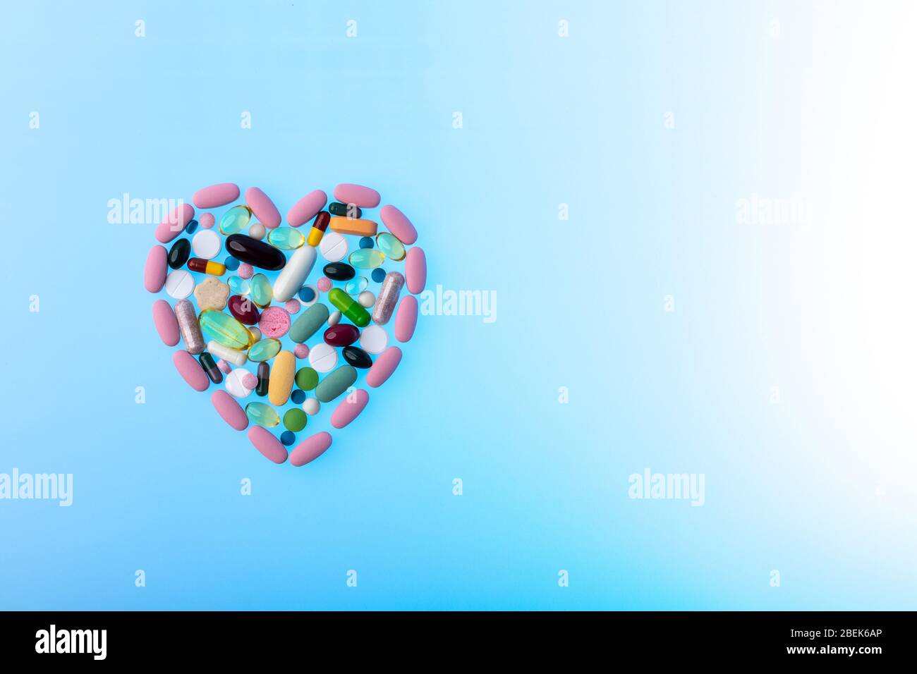 Pillole multicolore a forma di cuore su sfondo blu gradiente. Dose giornaliera di vitamine. Forma del cuore fatta di compresse, concetto di trattamento e. Foto Stock