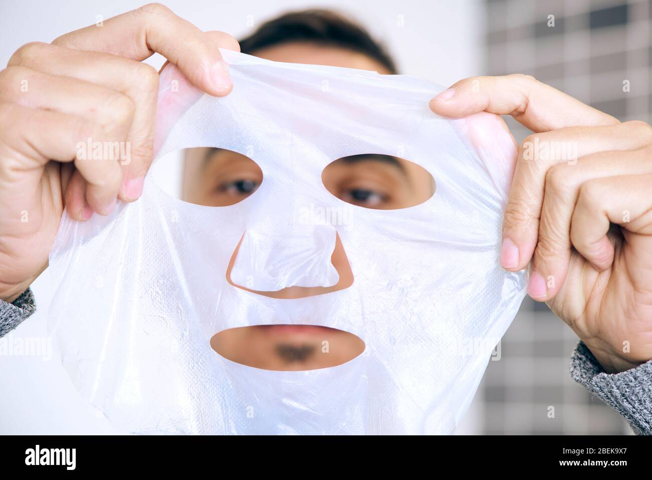 primo piano di un uomo caucasico che sta per applicare una maschera in foglio di bio-cellulosa al suo viso Foto Stock