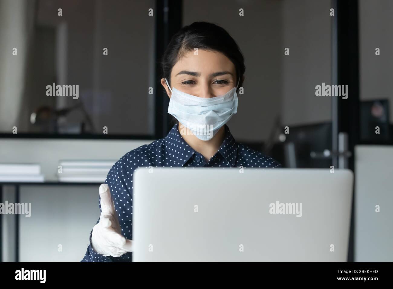 Dipendente femminile in maschera facciale consultare il cliente online Foto Stock