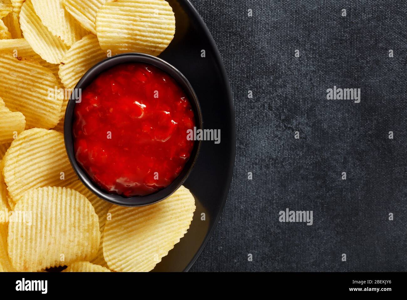 Patatine croccanti corrugate e salsa salsa salsa di salsa su un piatto nero con sfondo testurizzato nero. Vista superiore macro con spazio di copia. Foto Stock