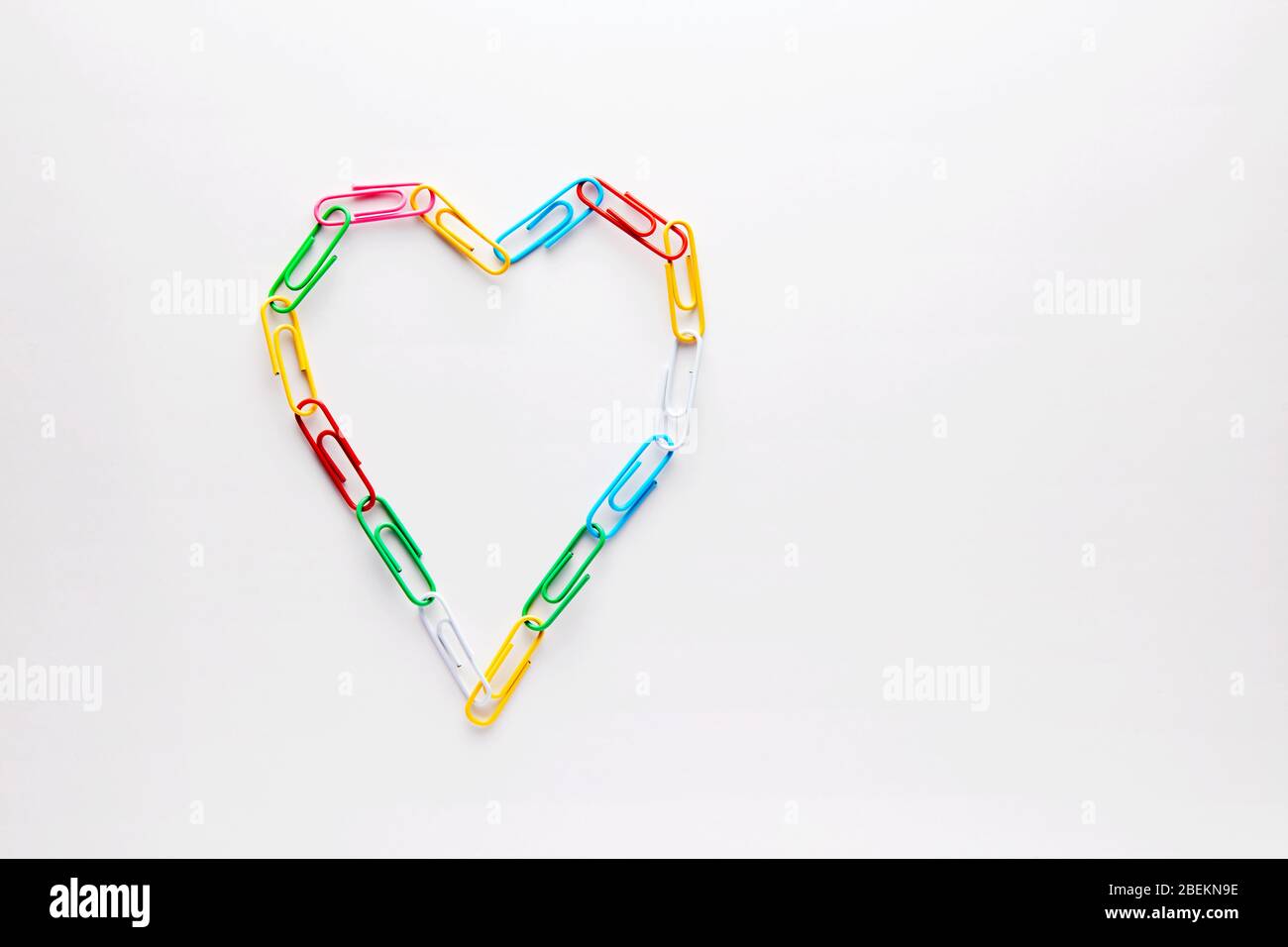 Clip di carta colorate disposte a forma di cuore su sfondo bianco. Concetto di primo amore a scuola Foto Stock