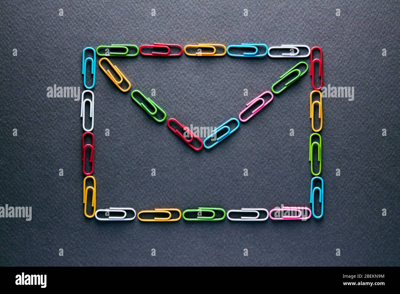 Clip per carta colorate progettate come busta su sfondo nero. Concetto di comunicazione con lettera o posta. Foto Stock